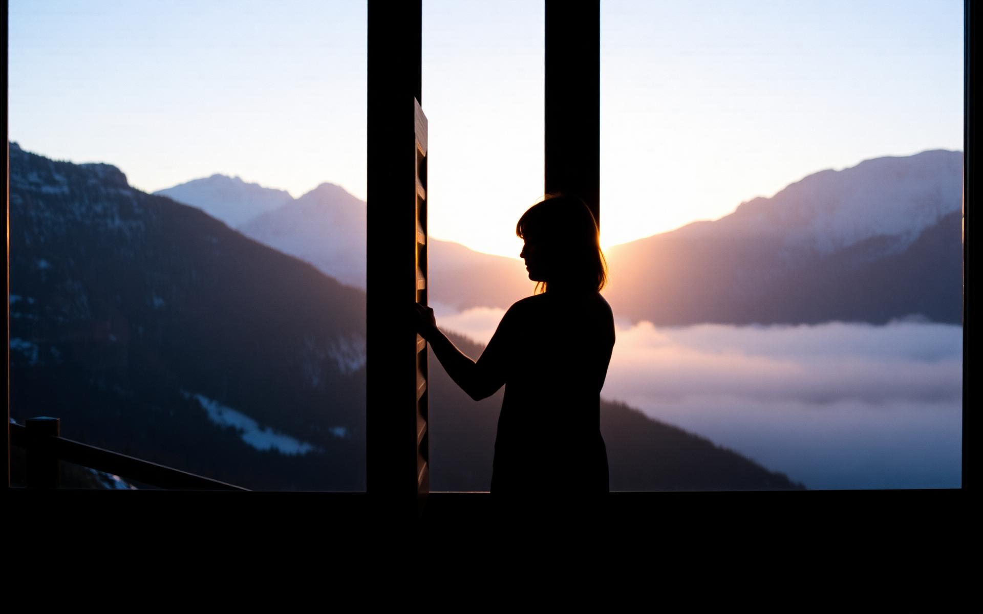 Silhouette à la fenêtre d'un refuge devant les sommets à l'aube